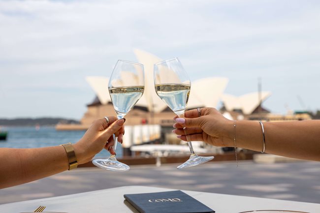 Wine glasses raised on Como's harbour terrace with the Sydney Opera House behind